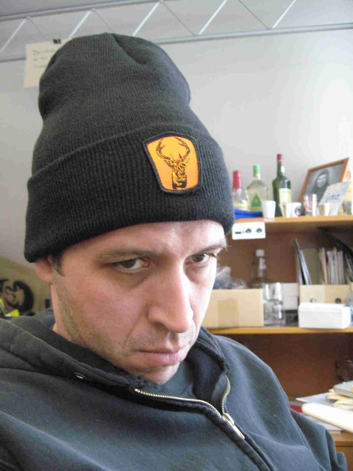 Headshot shot of a person with a grumpy face and wearing a stocking cap, in an office setting